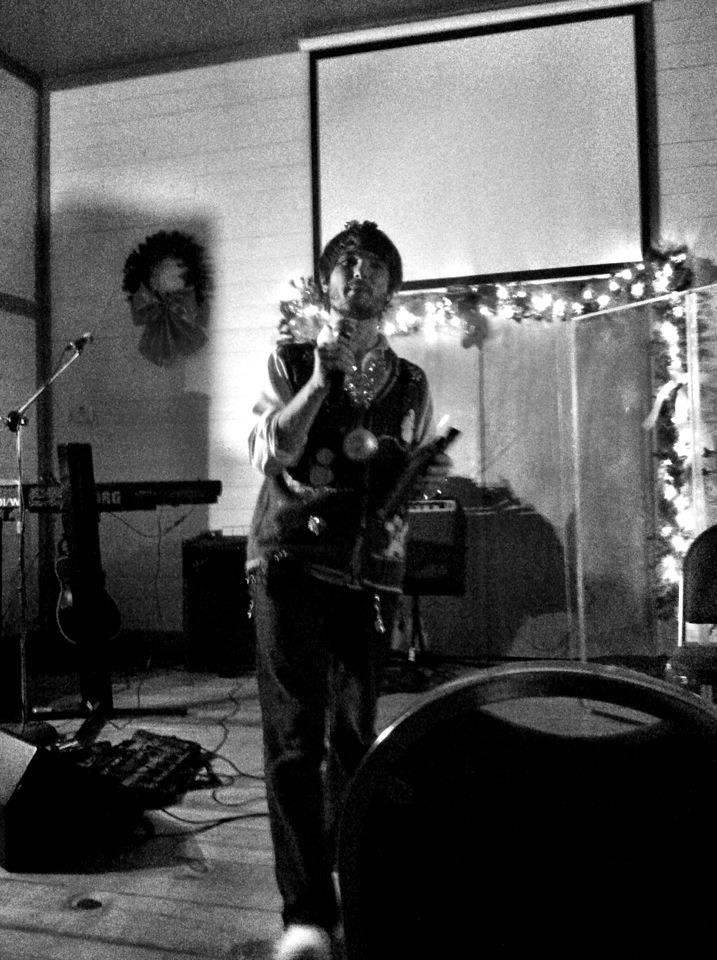 Black-and-white shot of Chris Ulery speaking on stage with holiday lights