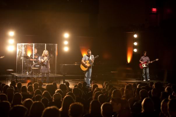 Chris Ulery performing with friends on a concert stage under warm lights