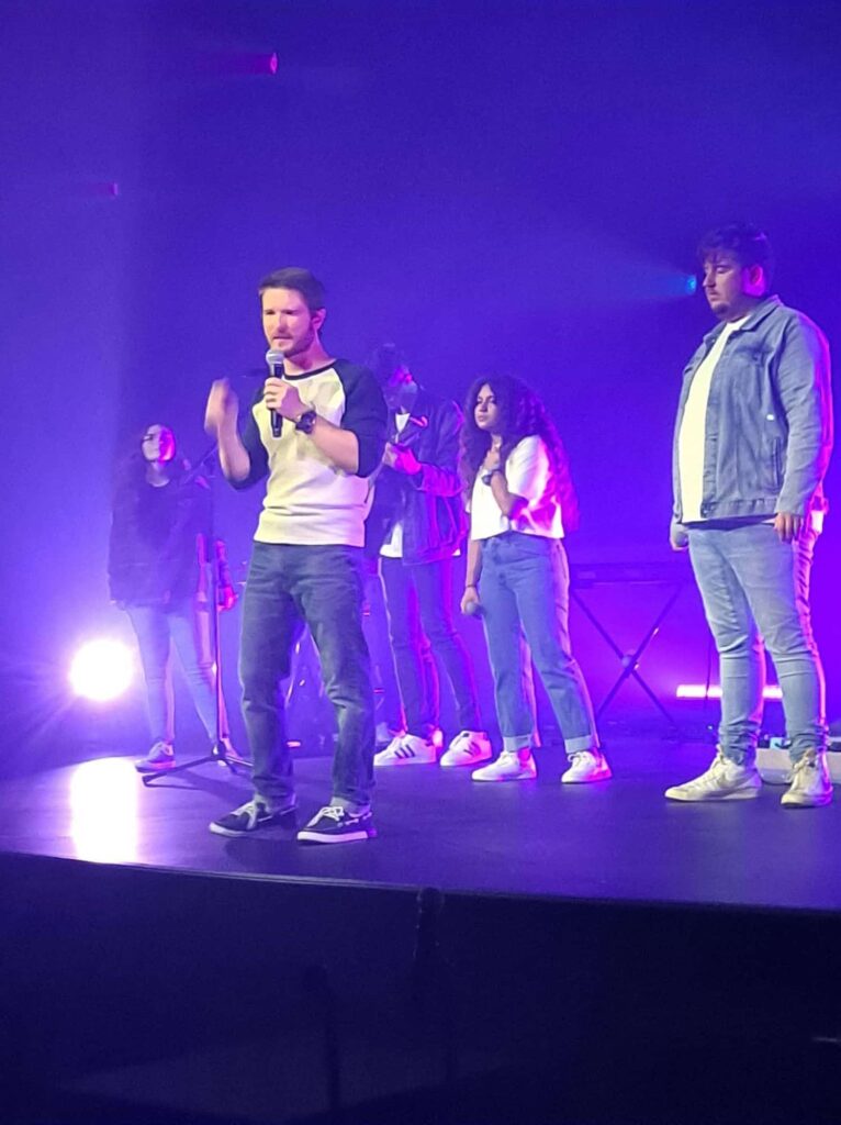 Chris Ulery gesturing as he speaks, with youth lined up on stage behind him