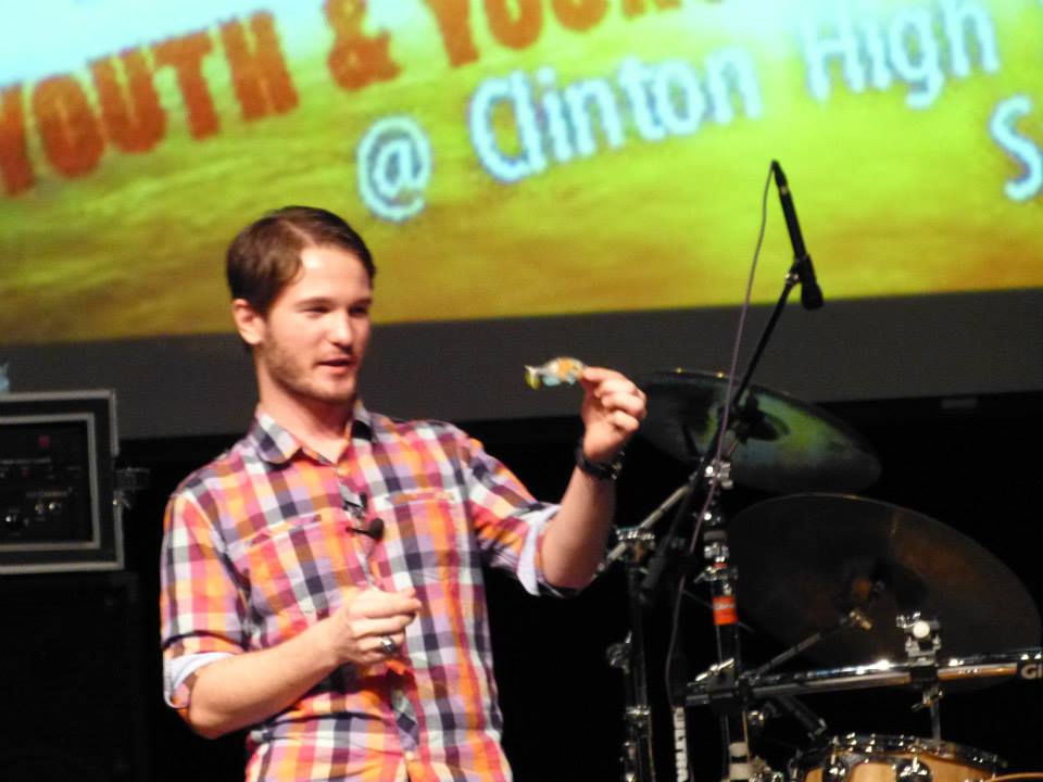 Chris Ulery holding up an object while speaking at a Clinton High School youth event