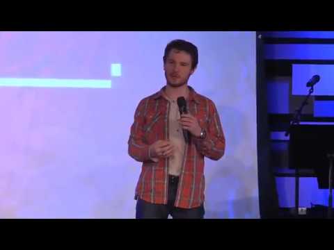 Chris Ulery in a red plaid shirt speaking before a bright blue backdrop