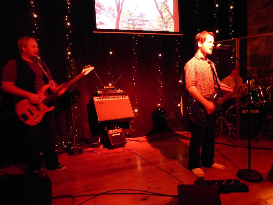 Chris Ulery playing guitar alongside a bassist on a red-lit stage