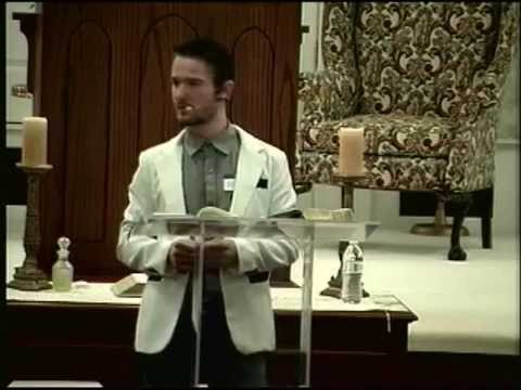 Chris Ulery preaching from a clear pulpit in a white jacket