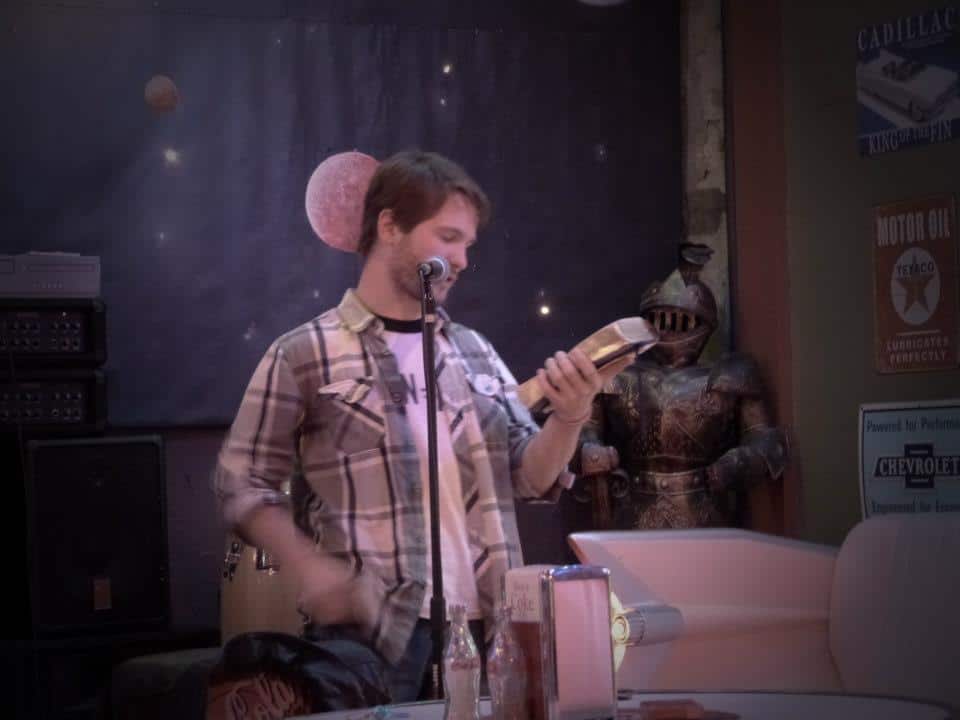 Chris Ulery reading from a Bible at a microphone in a casual venue