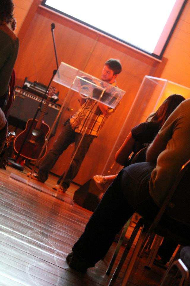 Chris Ulery speaking at an acrylic pulpit in warm orange light