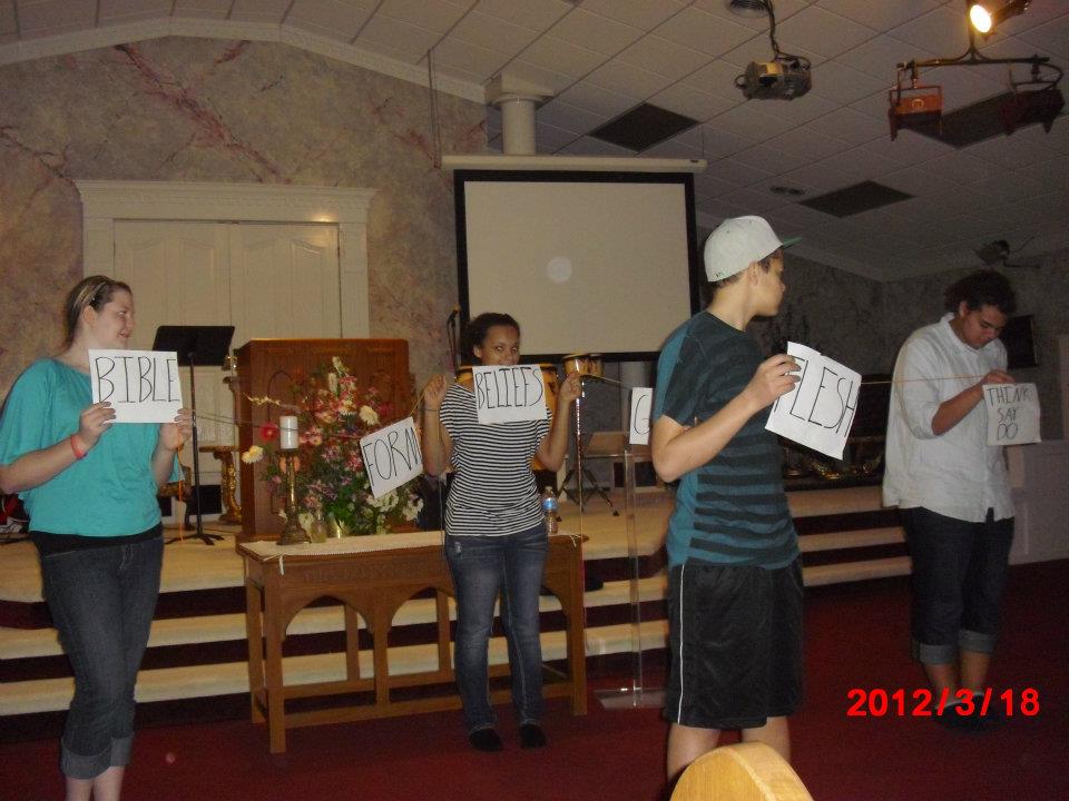 Teens holding handwritten signs at the front of a church at a Chris Ulery event