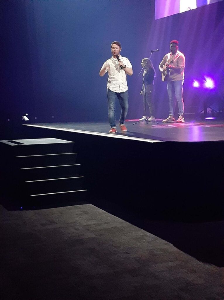 Chris Ulery speaking on the main stage at Victory Church in Tulsa with worship leaders behind him