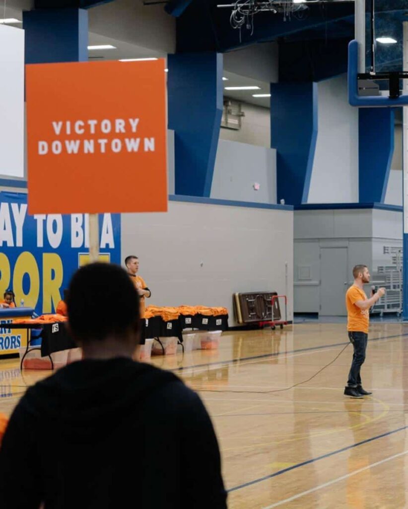 Chris Ulery speaking at a Victory Downtown community outreach event in a gym