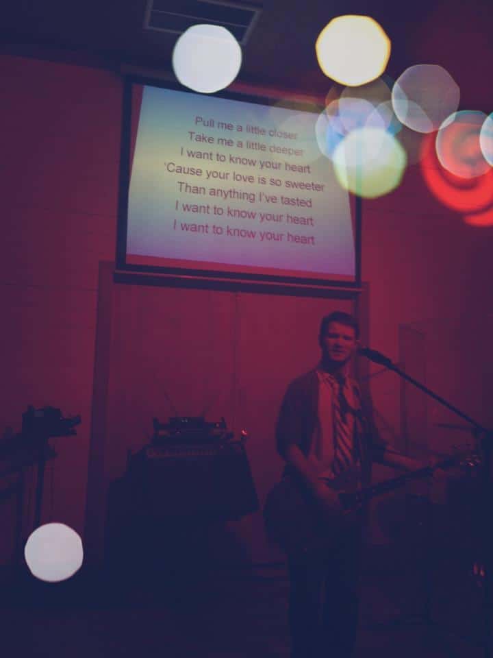 Worship song lyrics on a screen above a dim stage at a Chris Ulery event